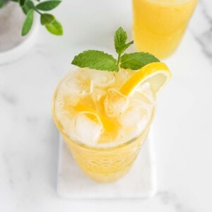 An overhead picture of lemonade in a clear glass with ice, a sprig of mint, and a sliced lemon