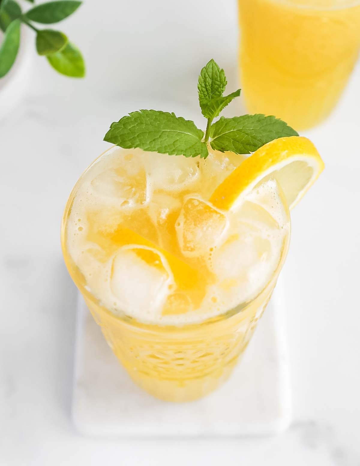 An overhead picture of a glass filled with yellow lemonade, ice, and a sprig of mint with a lemon slice on the edge