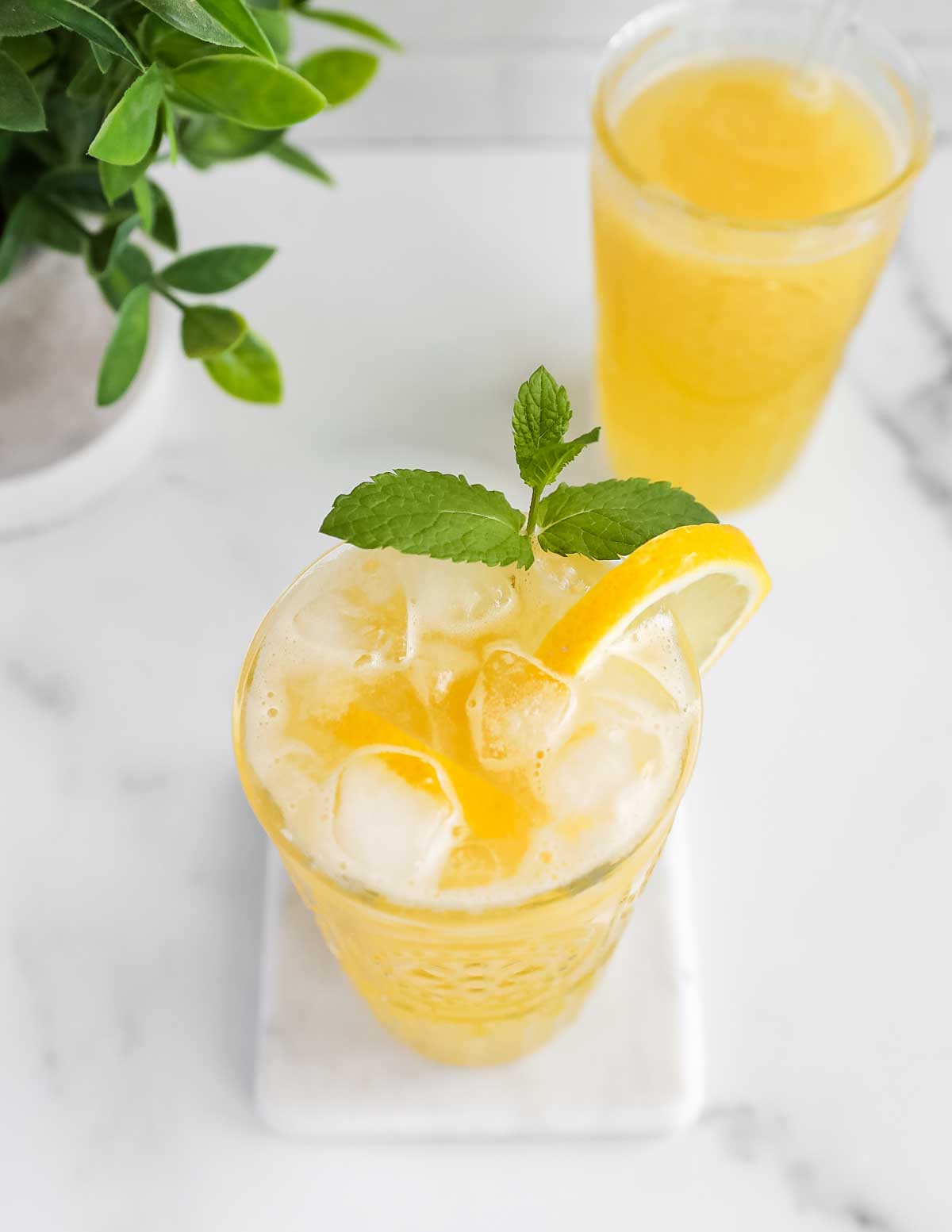 A clear glass filled with yellow lemonade, ice, sprig of green mint, and a lemon slice.