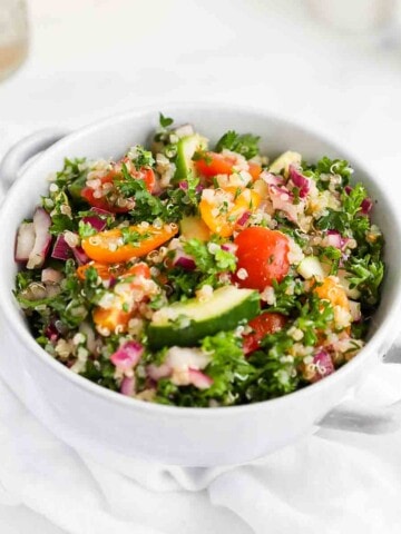 A light blue bowl filled with parsley, quinoa, tomatoes, onion, and cucumbers