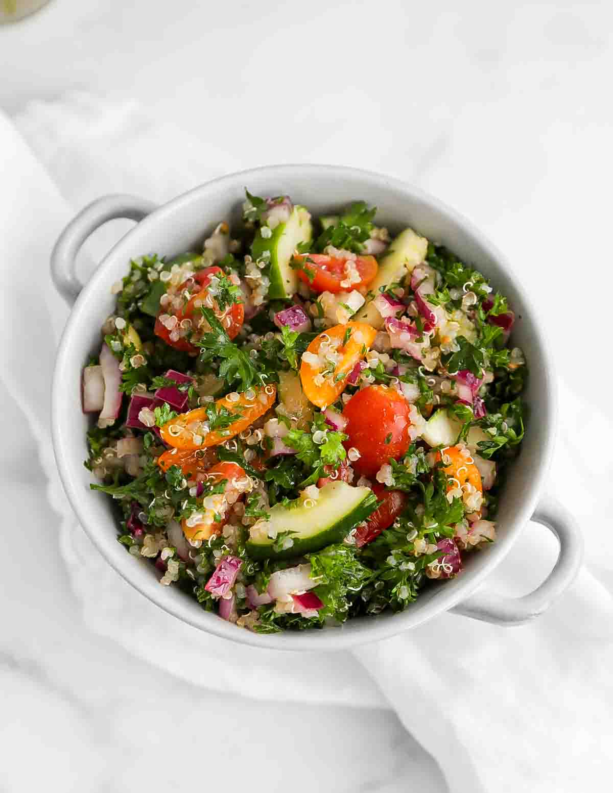 an overhead picture of a bowl filled with quinoa and chopped vegetables including: tomatoes, onion, cucumbers, and parsley