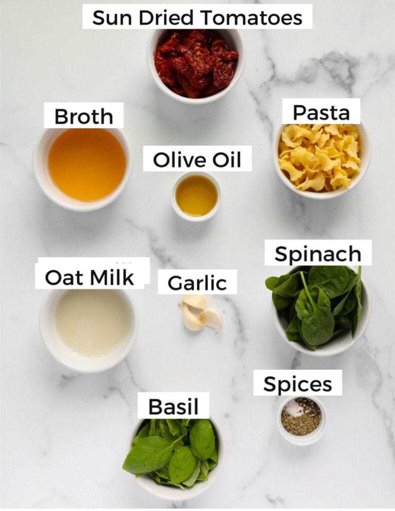 Small white bowls with ingredients that are labeled including, "sun dried tomatoes, broth, olive oil, pasta, oat milk, garlic, spinach, basil, spices.