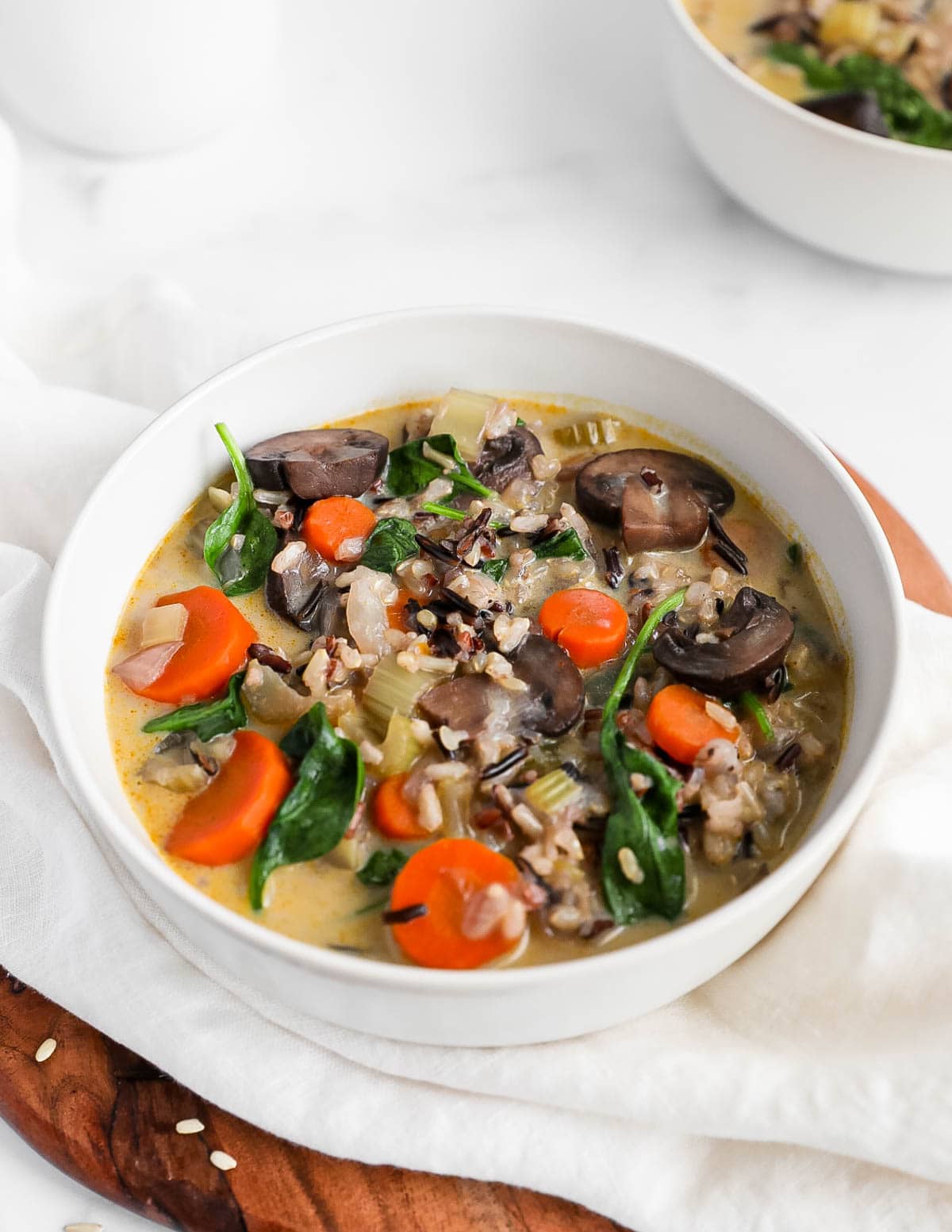 A bowl of vegetable and rice soup with mushrooms, carrots, spinach.