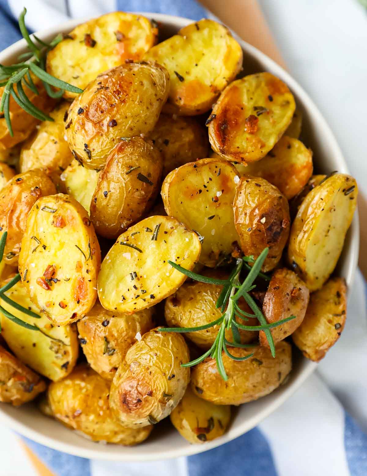 A close up image of sliced and roasted potatoes with seasoning on them inside of a bowl.