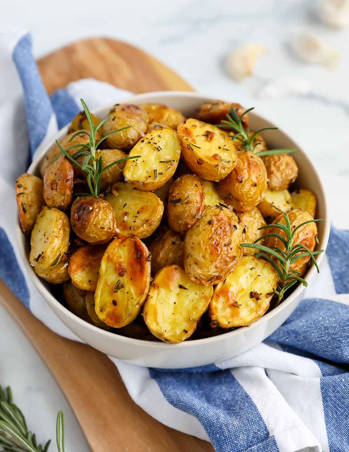 Golden yellow baby potatoes in a large white bowl with fresh rosemary on top.