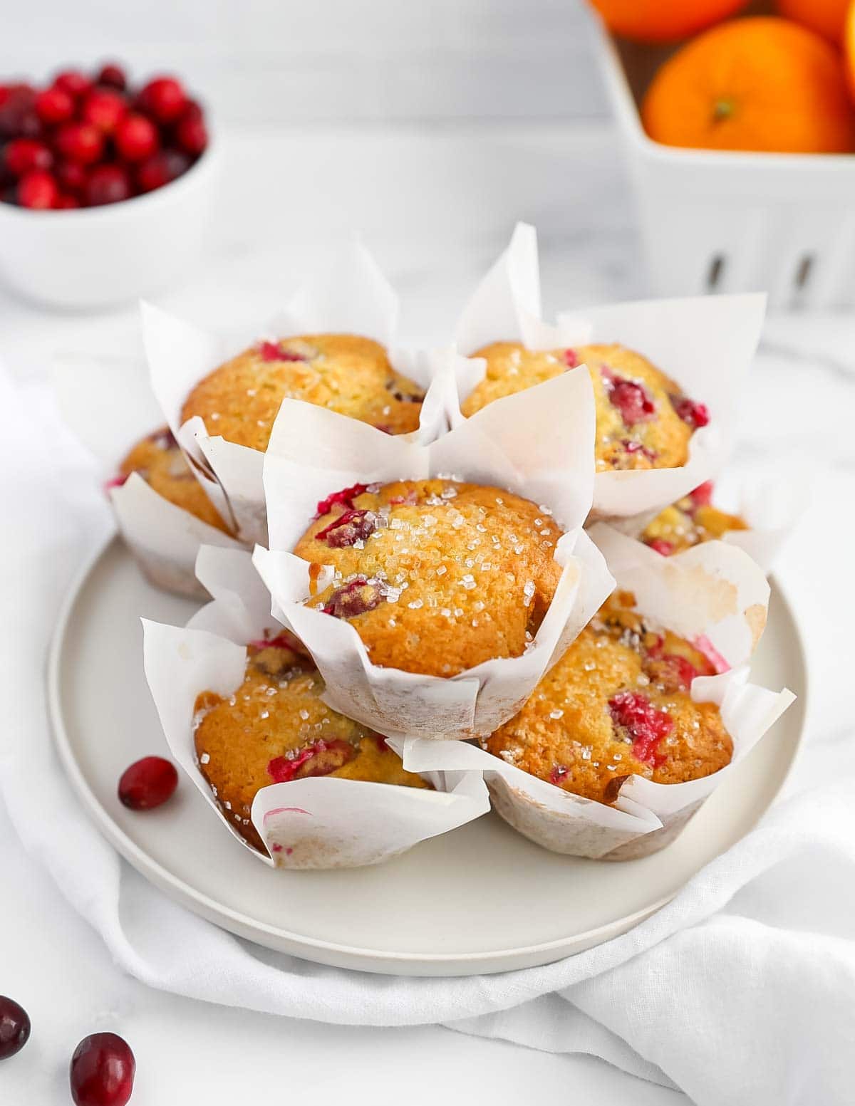 Fresh muffins wrapped in white parchment paper in a stack on a white dish.