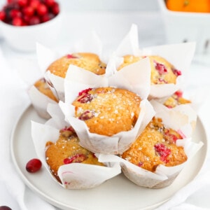 Muffins wrapped in parchment paper stacked on top of a white plate.
