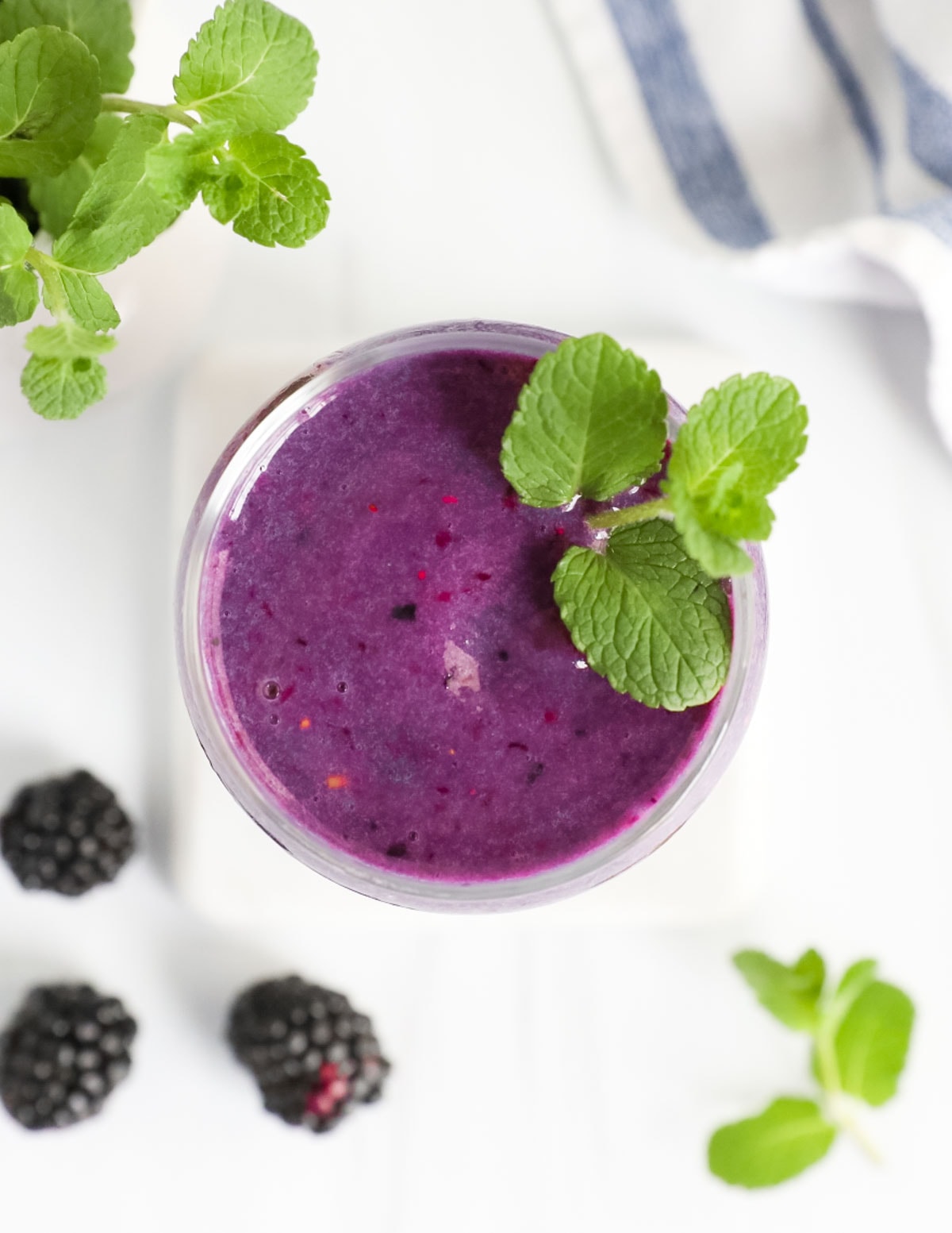 A clear cup with a purple smoothie inside and fresh mint leaves on top of the smoothie.