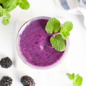 An overhead image of a bright purple smoothie in a clear cup with fresh mint on top.