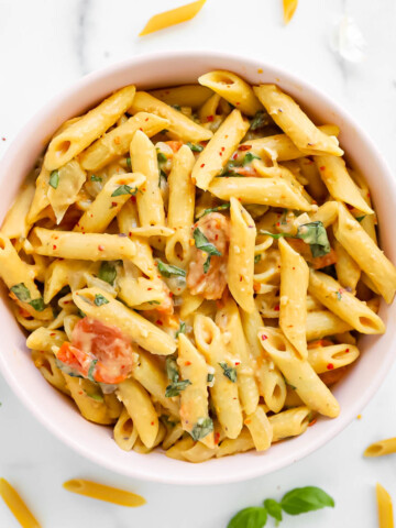 A pink bowl filled with penne pasta and creamy sauce.
