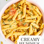A bowl filled with cooked penne noodles covered in a creamy sauce, chopped basil, and crushed red pepper flakes.