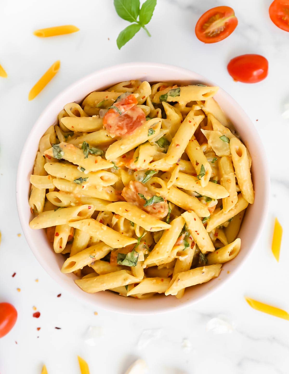 A pink bowl filled with penne pasta that is covered in a creamy sauce.