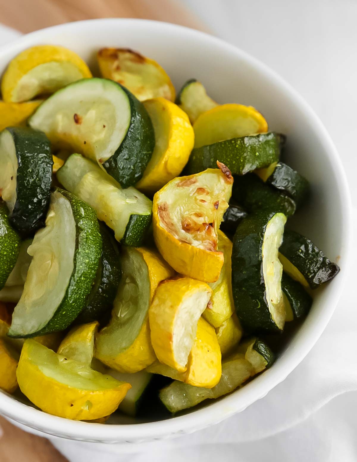 A close up image of cooked yellow squash and zucchini squash in a white bowl.