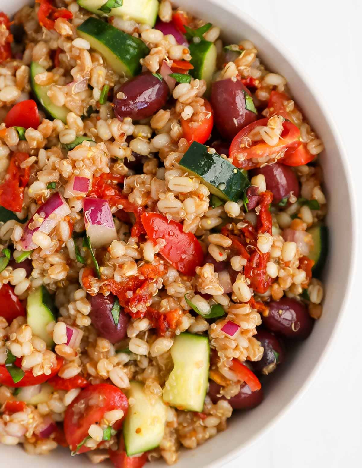 A close up picture of vegetables, cooked grains, and olives.