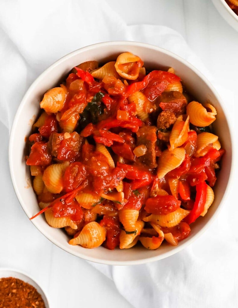 A white bowl with pasta, sauce, and sausage inside.