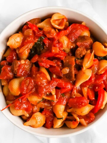 A close up picture of pasta shells, sauce, sausage, and peppers.