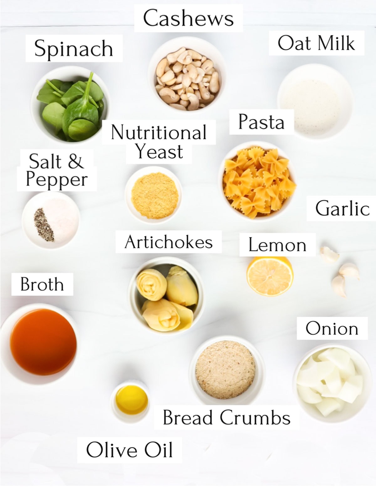 Labeled ingredients in white bowls including: cashews, spinach, oat milk, nutritional yeast, pasta, salt and pepper, artichokes, lemon, garlic, onion, broth, olive oil, bread crumbs, onion.