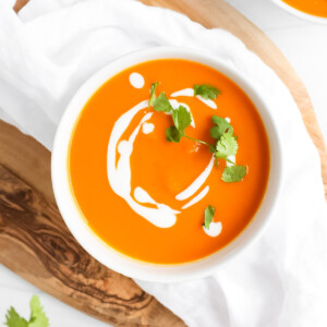 Orange soup in a white bowl that is topped with white coconut milk drizzle and fresh cilantro.