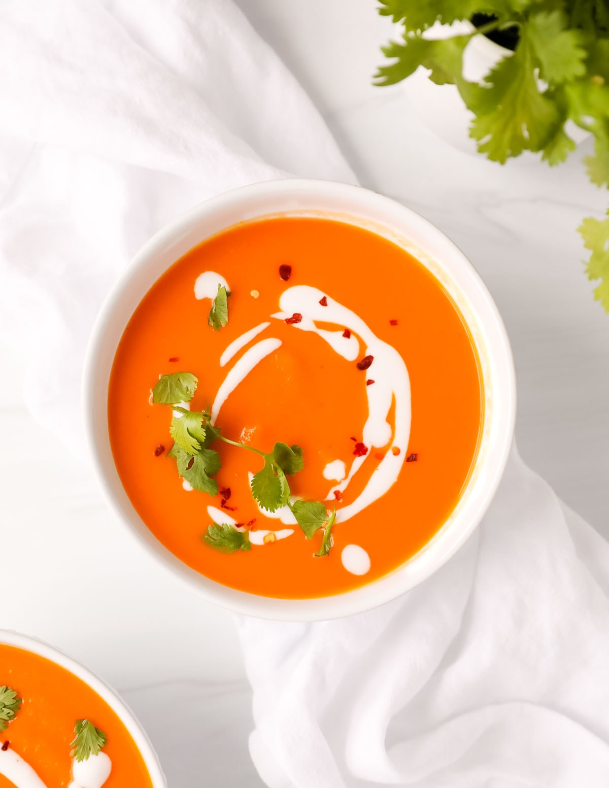 An overhead image of a bowl of carrot soup that is topped with coconut milk, cilantro, and red pepper flakes.