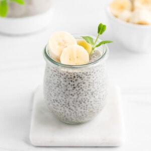 A glass jar filled with chia pudding with bananas and mint on top.