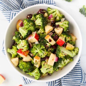 A bowl filled with fresh broccoli, apple slices, dried cranberries, and red onion.