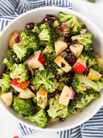 A bowl filled with fresh broccoli, apple slices, dried cranberries, and red onion.