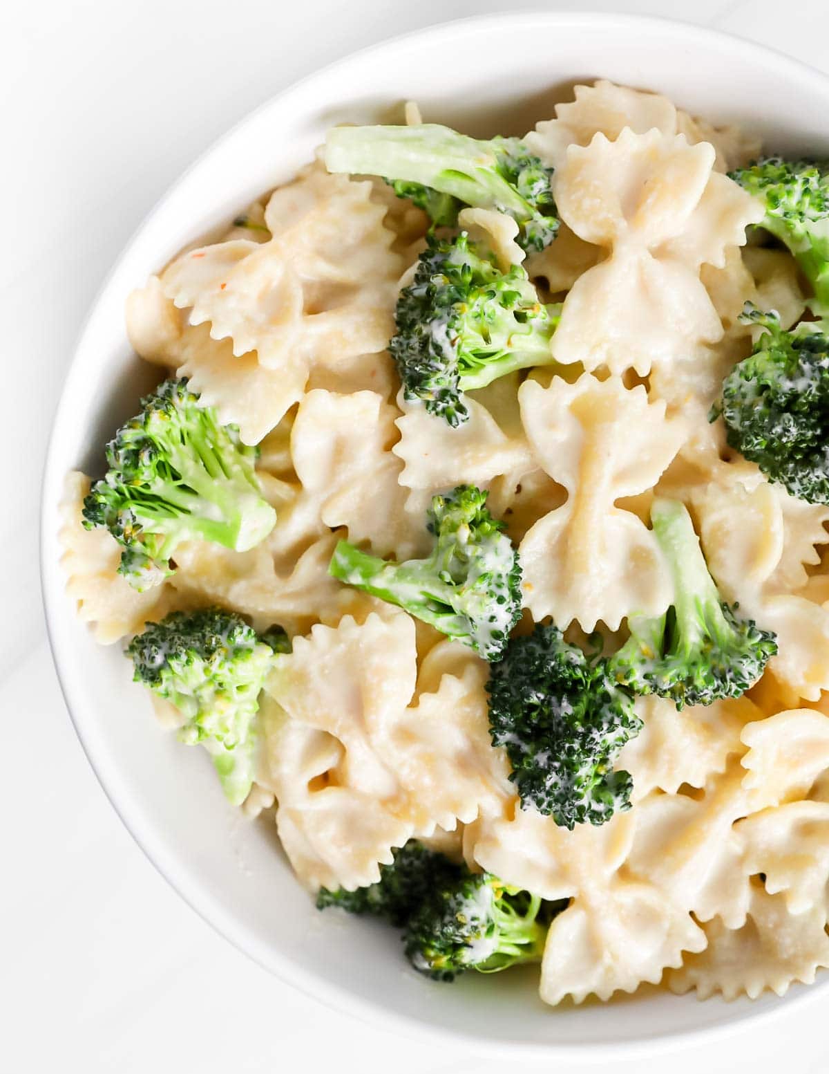 A close up picture of pasta in a white sauce with broccoli mixed in.