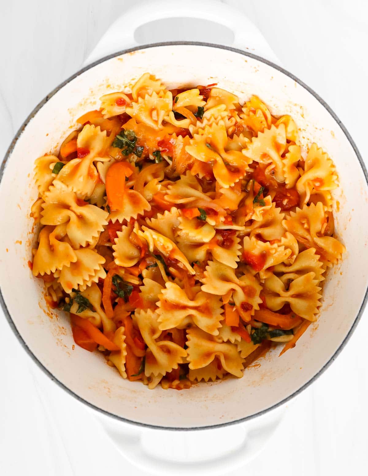 Pasta in a red sauce with vegetables in a large white pot.