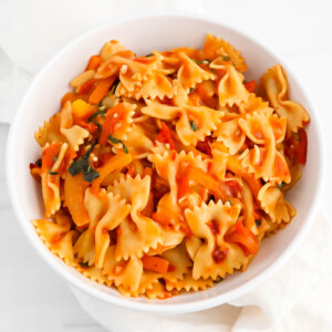 Bowtie pasta tossed in a thick red sauce in a white bowl.