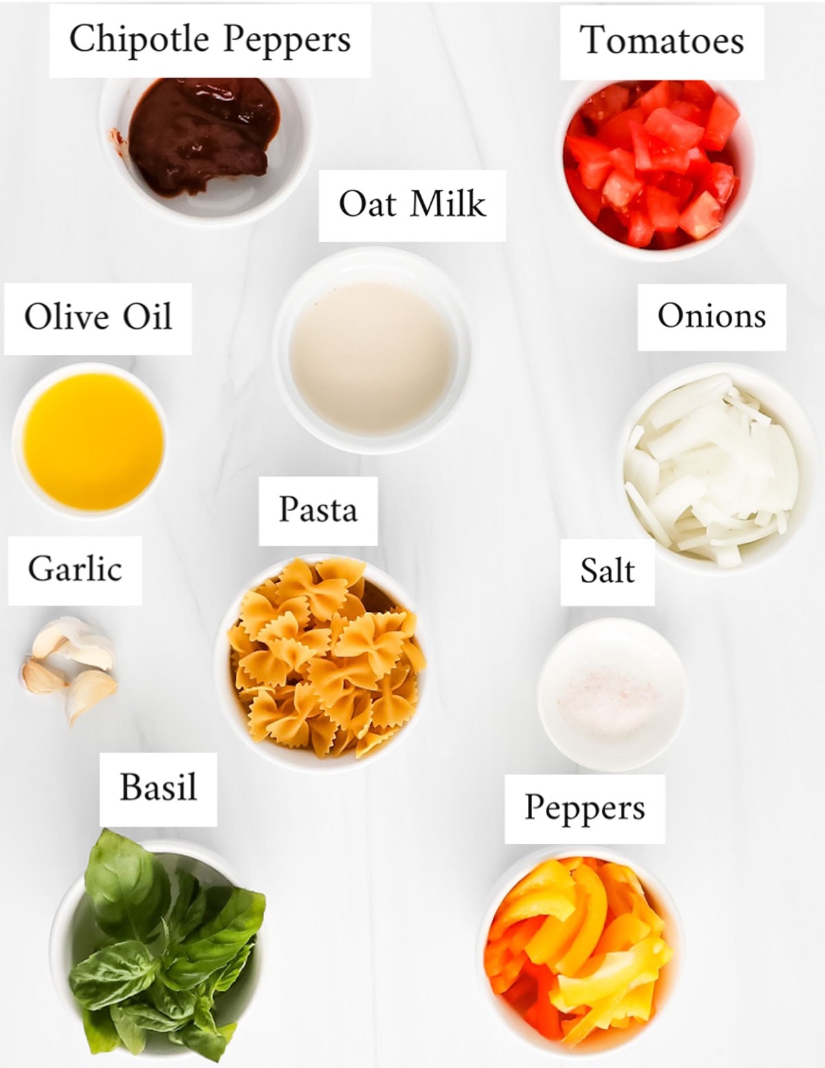 Labeled ingredients in small white bowls including: chipotle peppers, tomatoes, oat milk, olive oil, onions, pasta, garlic, salt, basil, peppers.