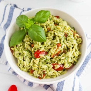 A bowl of orzo with pesto sauce, tomatoes, and fresh basil.