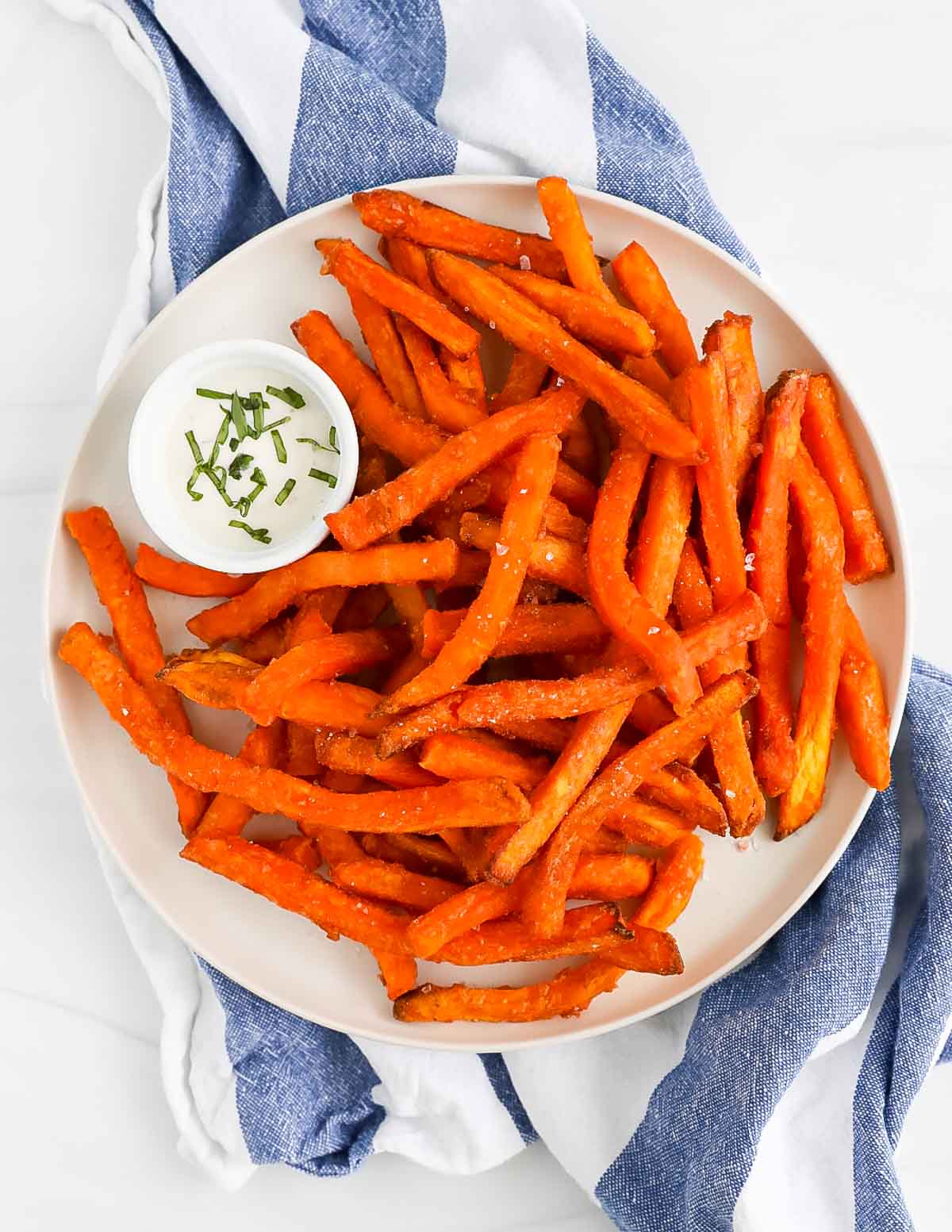 Sweet potato fries covered in salt on a white plate along with a white dish filled with ranch dressing.