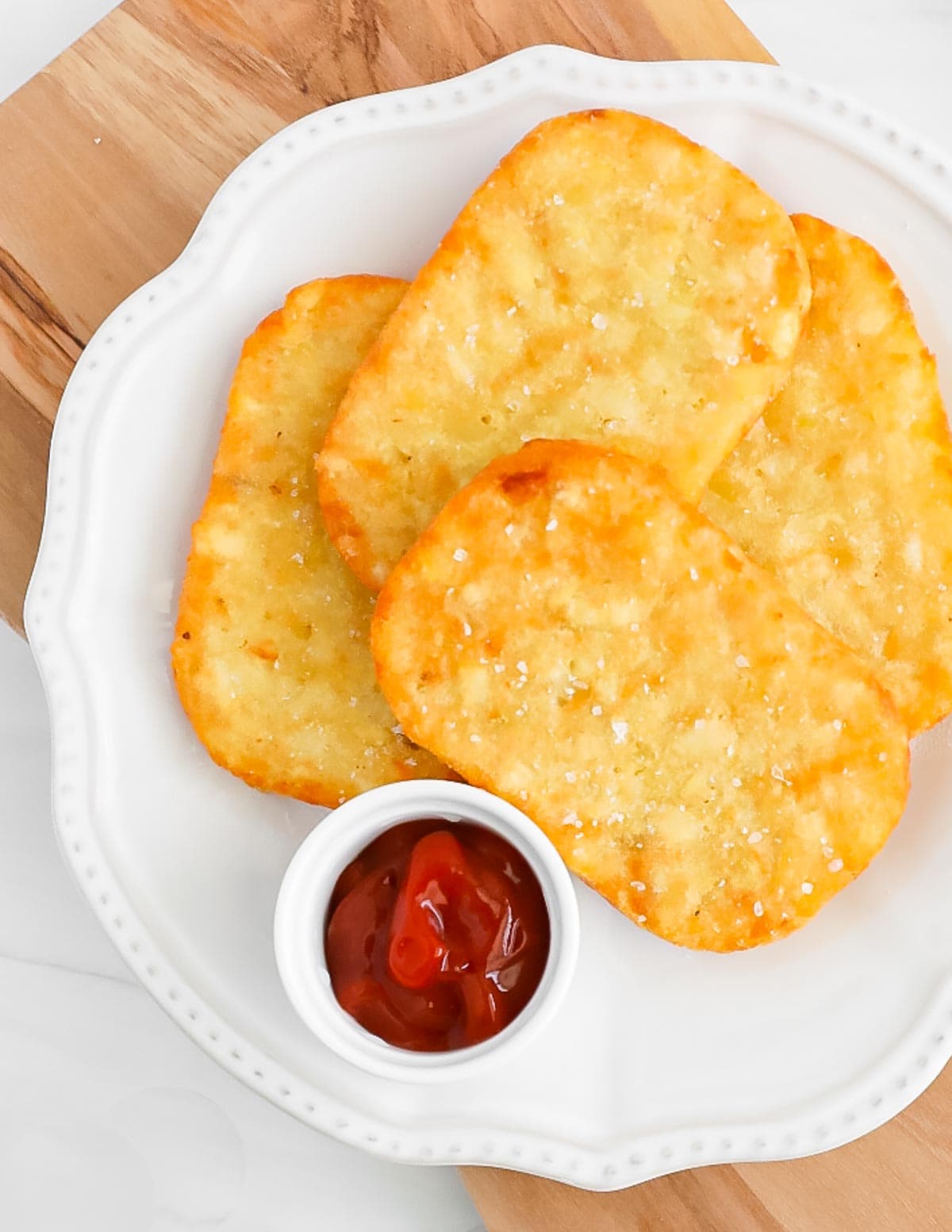 Four toasted hash browns on a white plate with a small bowl of ketchup.