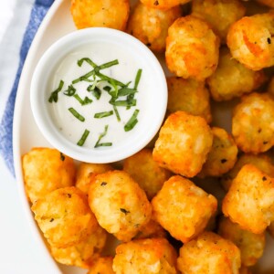Tater tots on a plate with a white dish filled with ranch dressing and fresh basil.