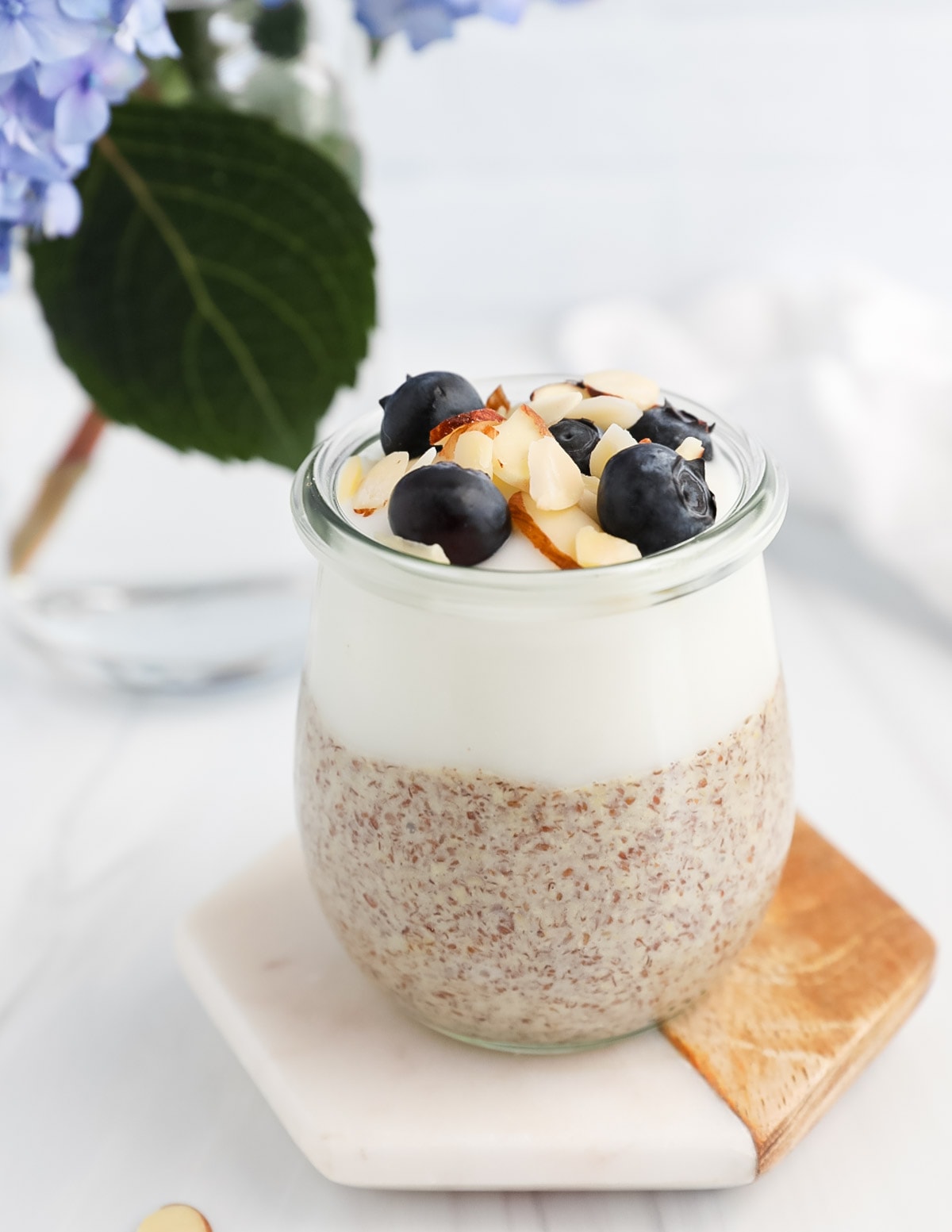A clear jar filled with half vanilla yogurt and half pudding with blueberries and almonds on top.