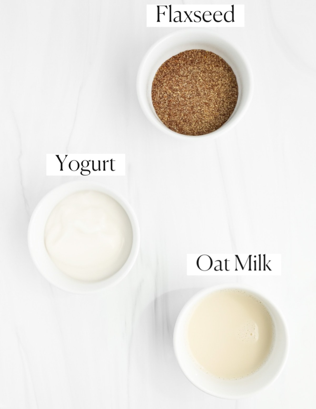 Three bowls filled with labeled ingredients including: flaxseed, yogurt, and oat milk.