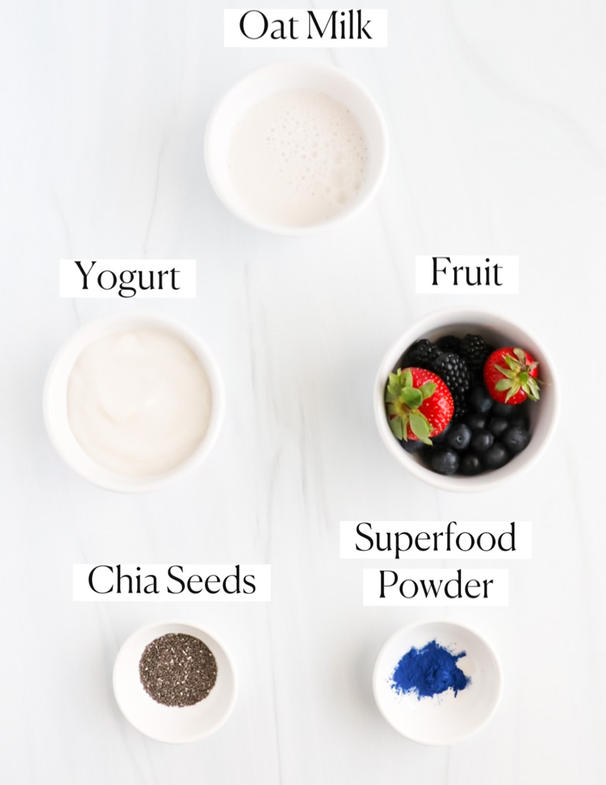 Labeled ingredients in small white bowls including: oat milk, yogurt, fruit, chia seeds, and superfood powder.