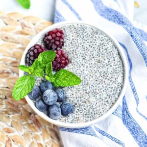 A white bowl filled with chia seed pudding. There are blackberries, blueberries, and fresh mint leave on top.