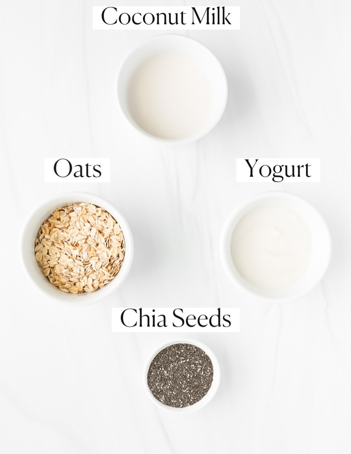 Labeled ingredients in small white bowls including: coconut milk, oats, yogurt, and chia seeds.