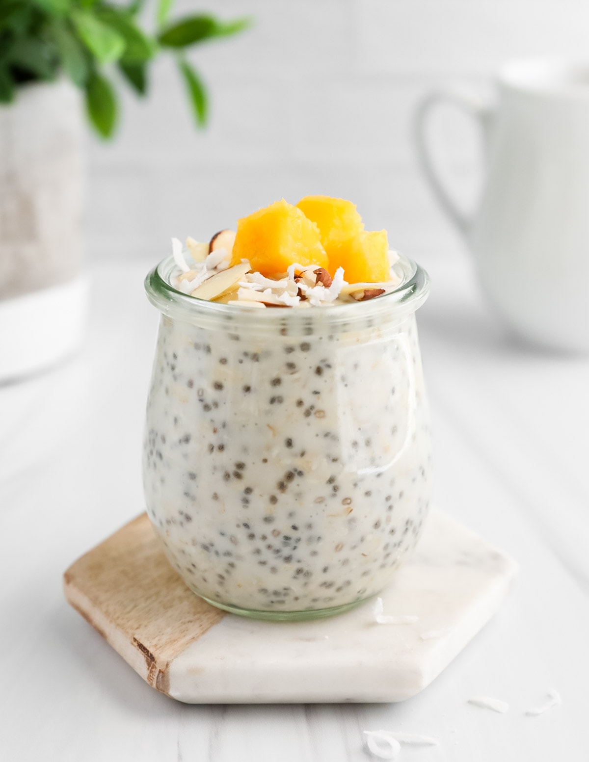 A jar of chia overnight oatmeal with mango, coconut flakes, and almonds on top.