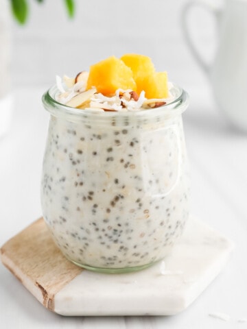 Overnight oatmeal in a jar with nuts, coconut flakes, and mango on top.