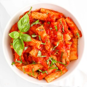 A white bowl filled with rigatoni covered in a red sauce and fresh basil.