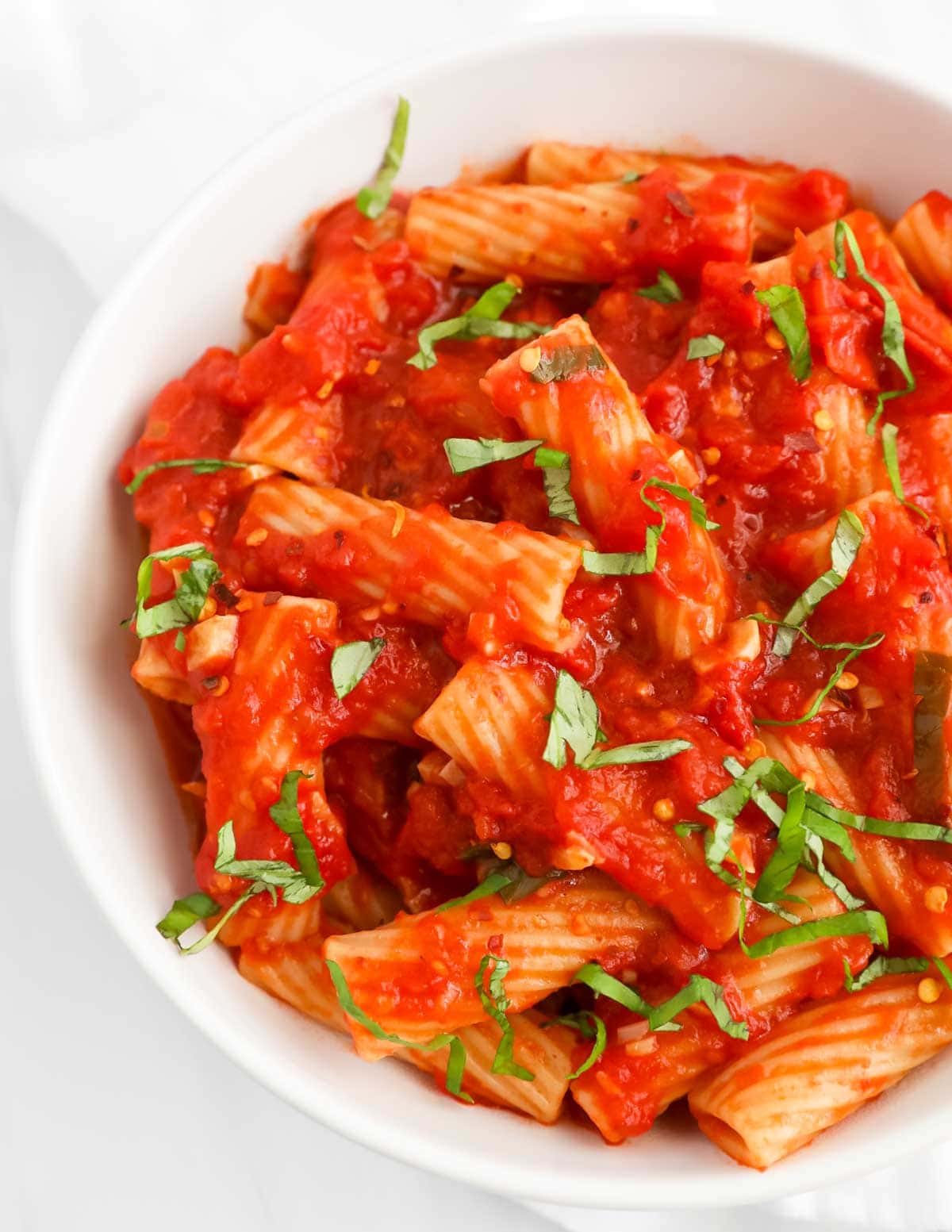 A close up picture of pasta in a red sauce that has chopped basil on top.