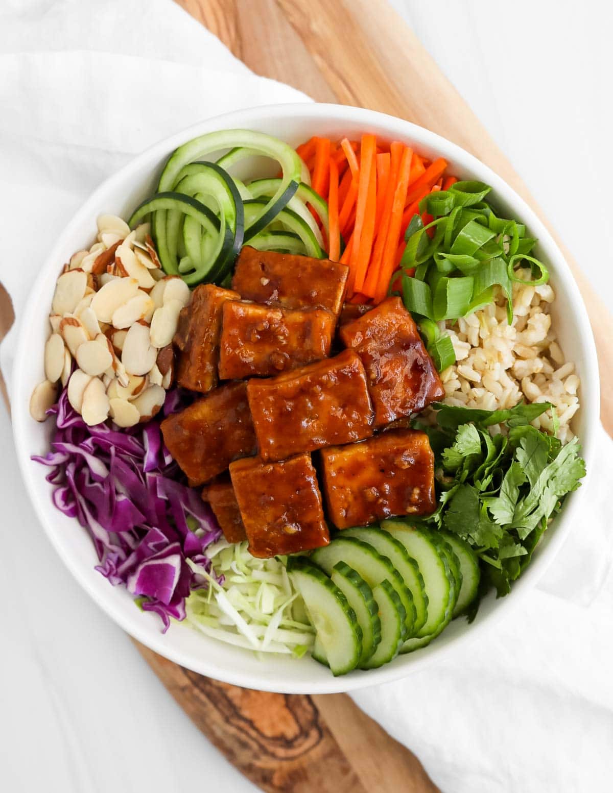 Tofu on a bed of vegetables such as carrots, cucumbers, green onions, cilantro, and cabbage, as well as rice and almonds.