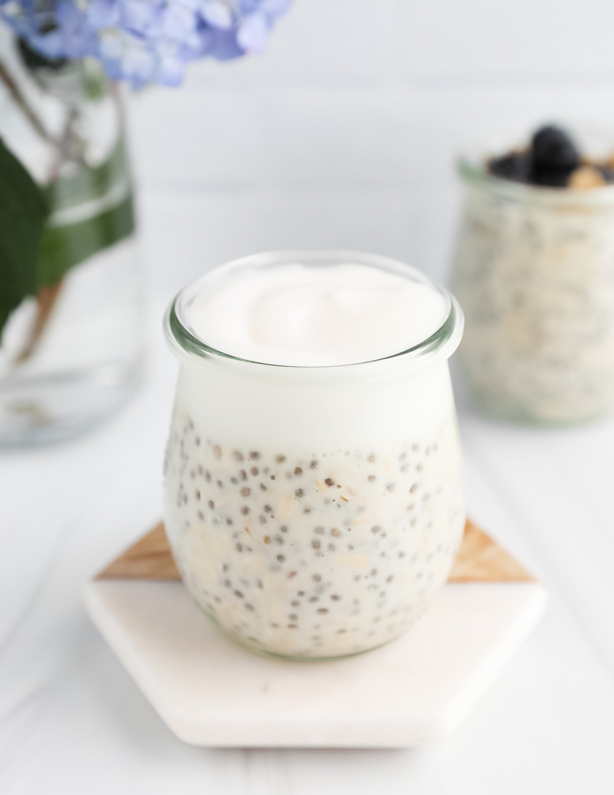 A clear jar of overnight oatmeal and yogurt sitting on a coaster.