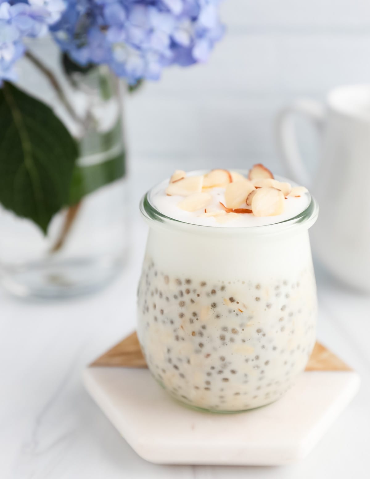 A glass jar on a coaster filled with overnight oats, yogurt, and shaved almonds on top.