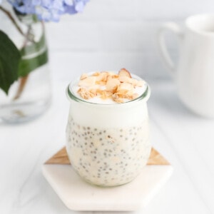 A clear jar filled with vanilla overnight oats with chia seeds that is topped with granola and nuts.