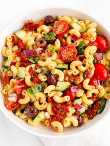 A veggie-filled pasta salad in a white bowl.