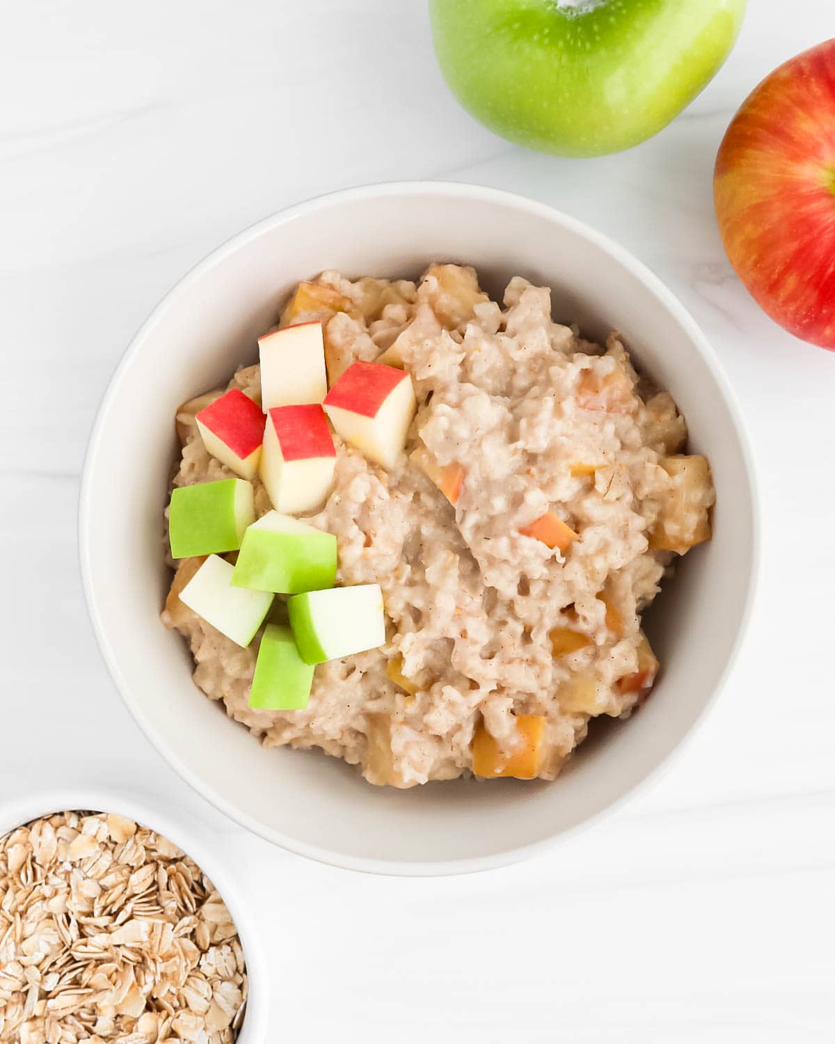 A bowl filled with cooked oatmeal and fresh apples.