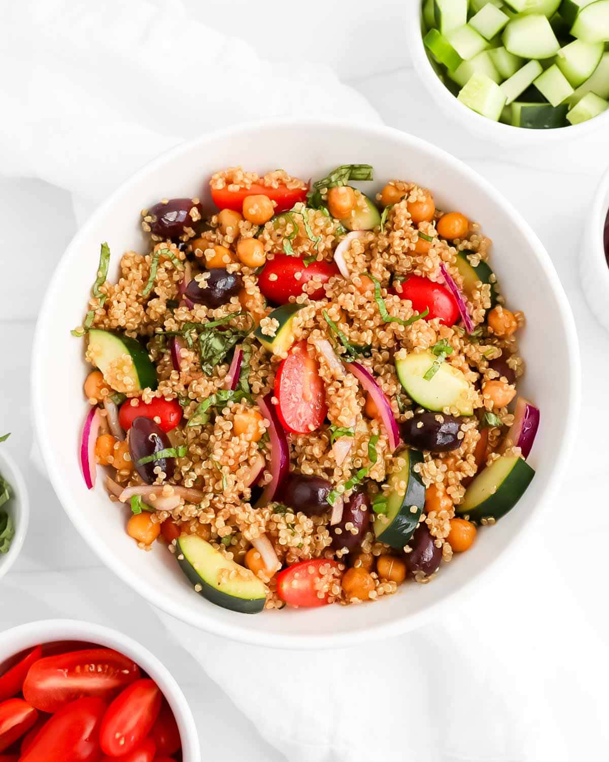A white bowl with a medley of Mediterranean Quinoa Salad with fresh basil on top.